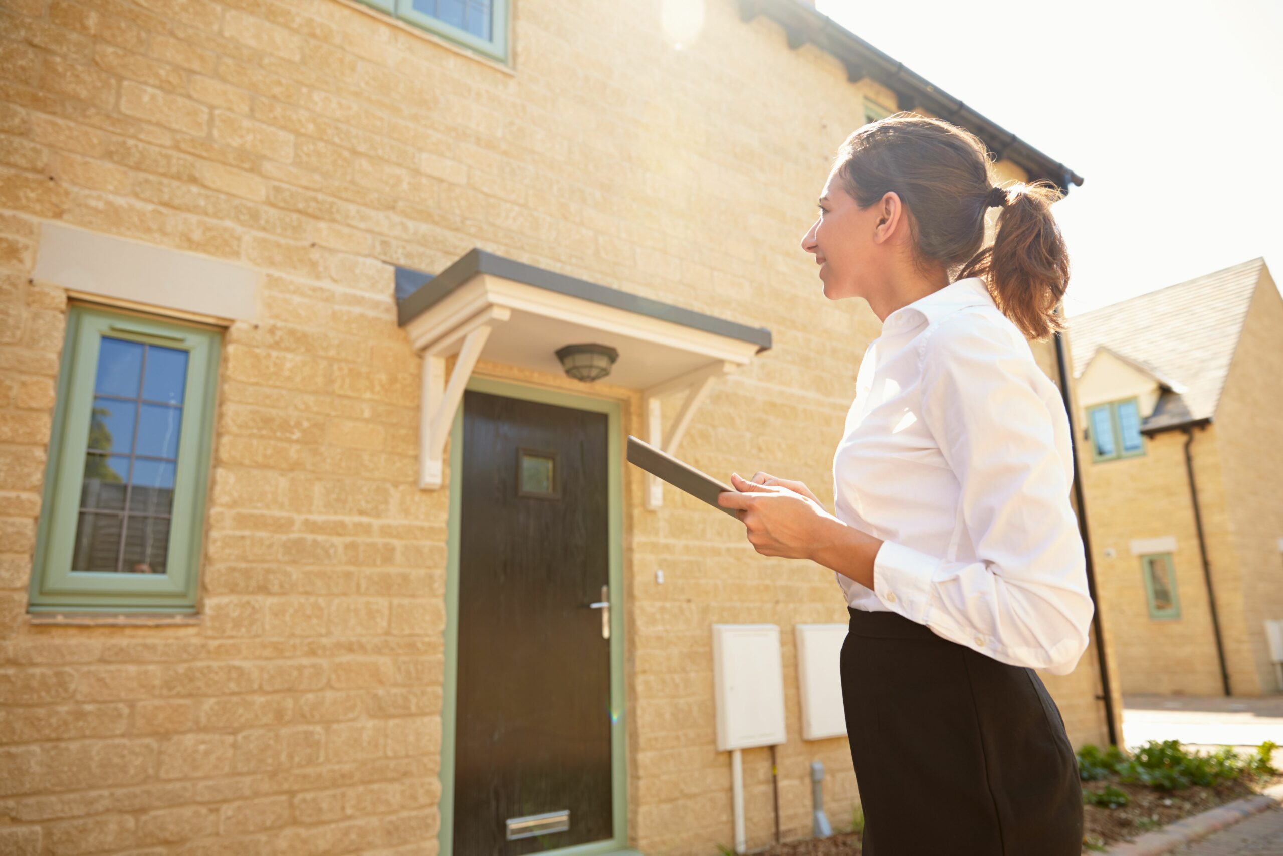 Using a home report. Female real estate agent looking at a house exterior.